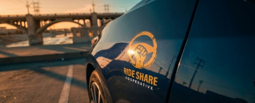 A driver standing on a city street at night next to a white rideshare vehicle